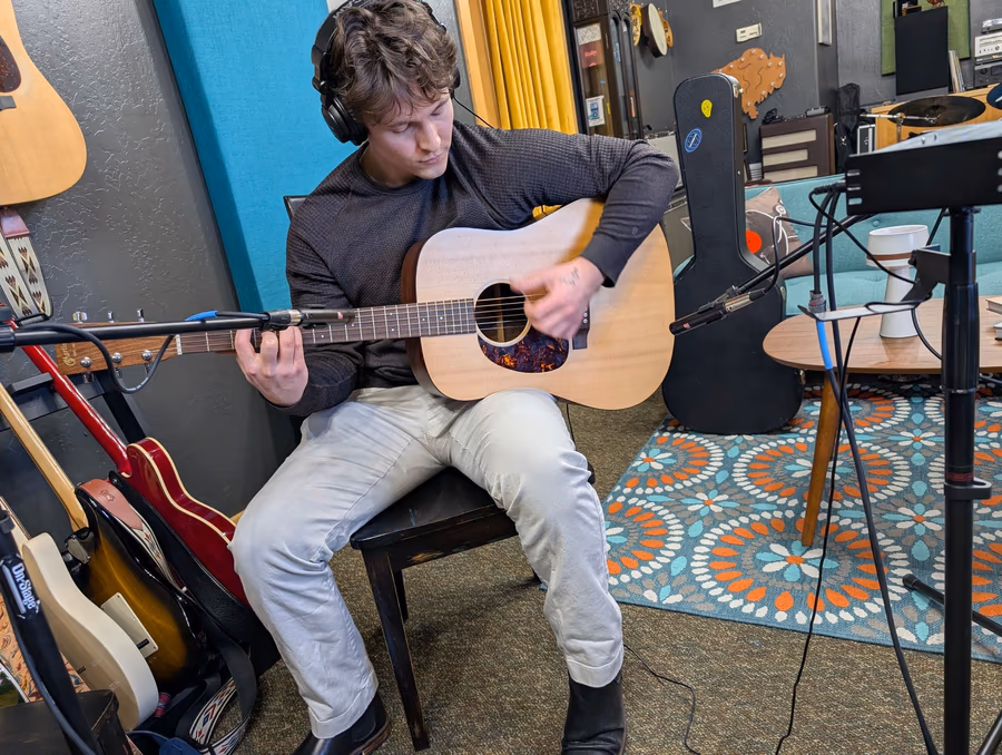 An acoustic guitarist recording with two microphones in the live room